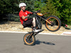 A person doing a wheelie on an orange Isinwheel Monster Pro Mid-Drive Electric Dirt Bike