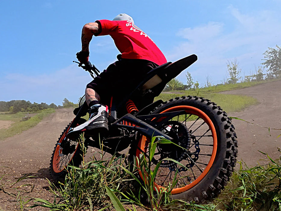 A person riding an Isinwheel Monster Pro Mid-Drive Electric Dirt Bike on a dirt track, back view
