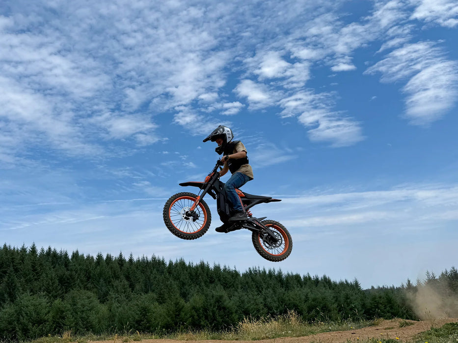 A rider in a high mid-jump on an orange Isinwheel Monster Pro Mid-Drive Electric Dirt Bike