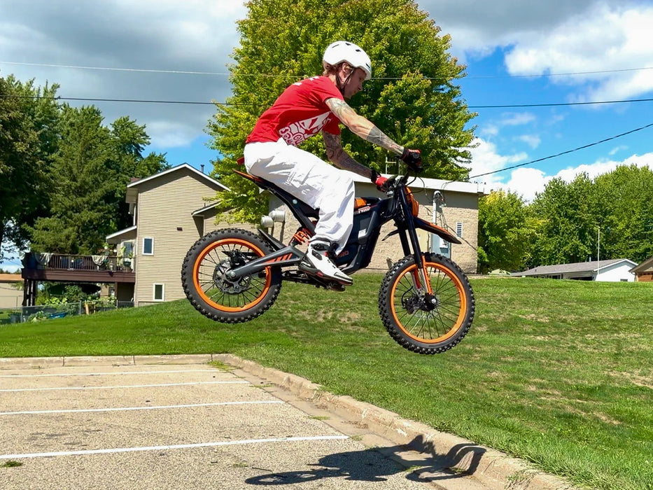 A rider doing a jump on an orange Isinwheel Monster Pro Mid-Drive Electric Dirt Bike