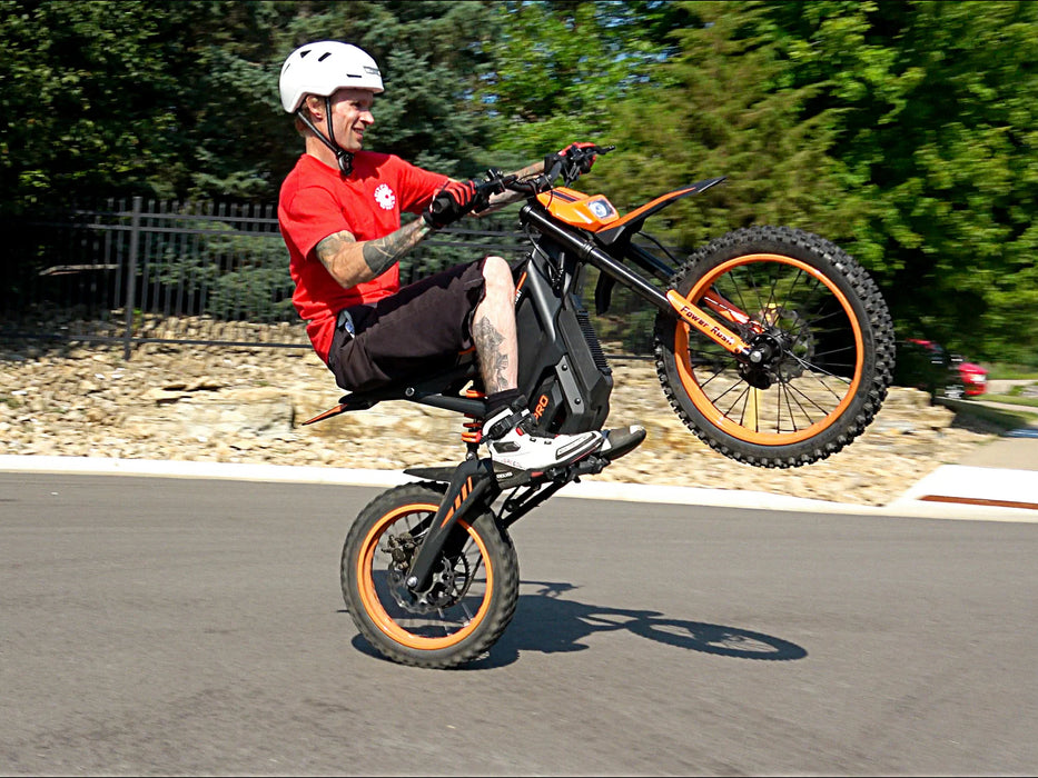 A person doing a wheelie on an orange Isinwheel Monster Pro Mid-Drive Electric Dirt Bike